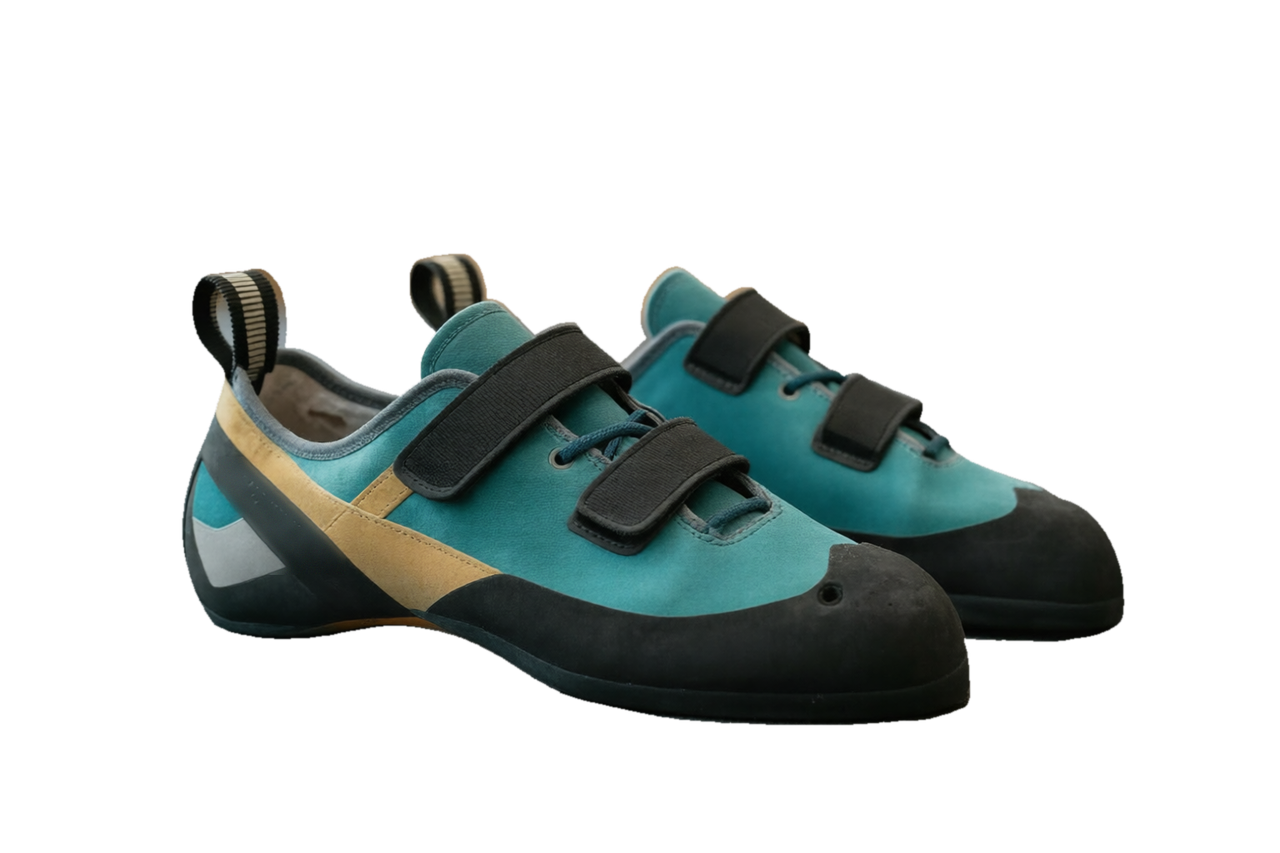 A clean pair of climbing shoes, teal uppers with a tan panel and black rubber, resting on the counter in front of the machine